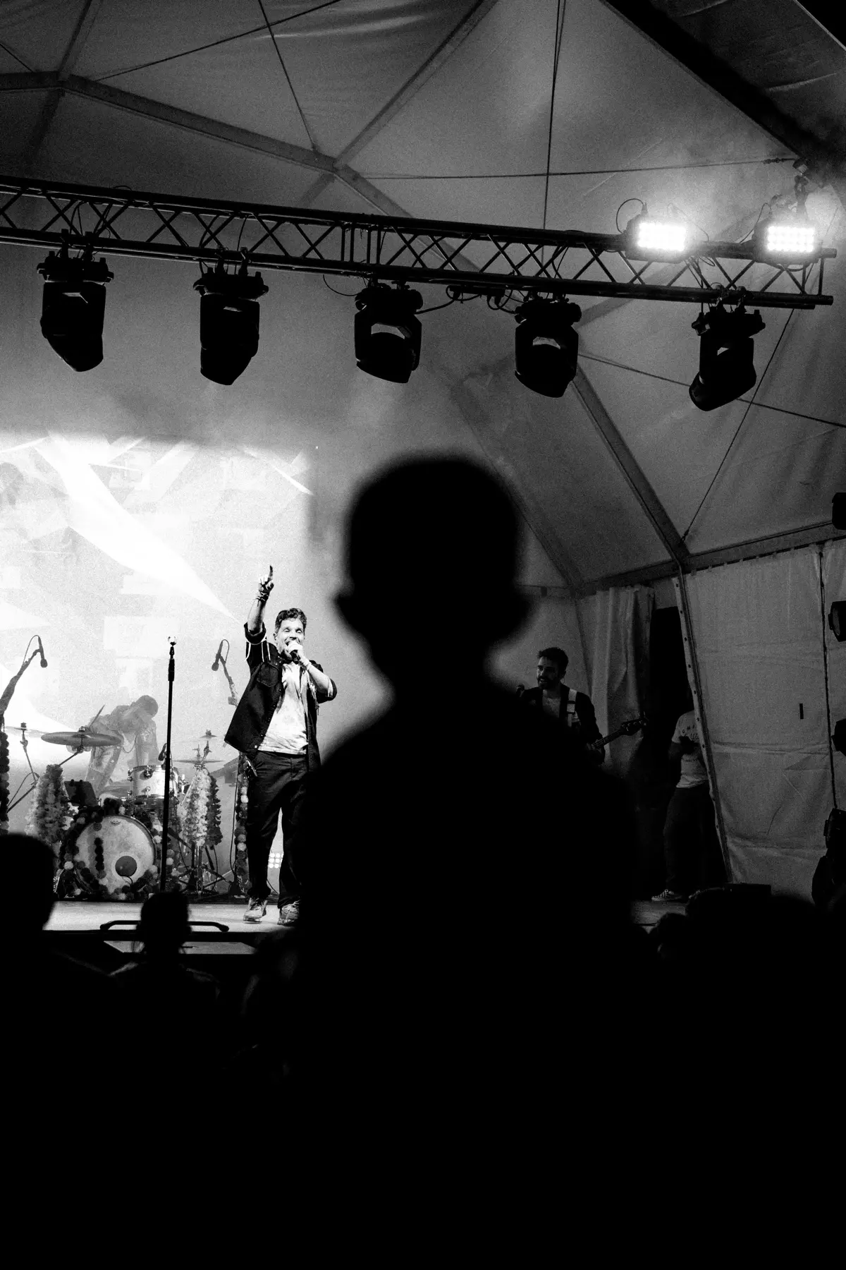 Vocalista em palco com banda, silhueta do público em primeiro plano, fotografia a preto e branco
